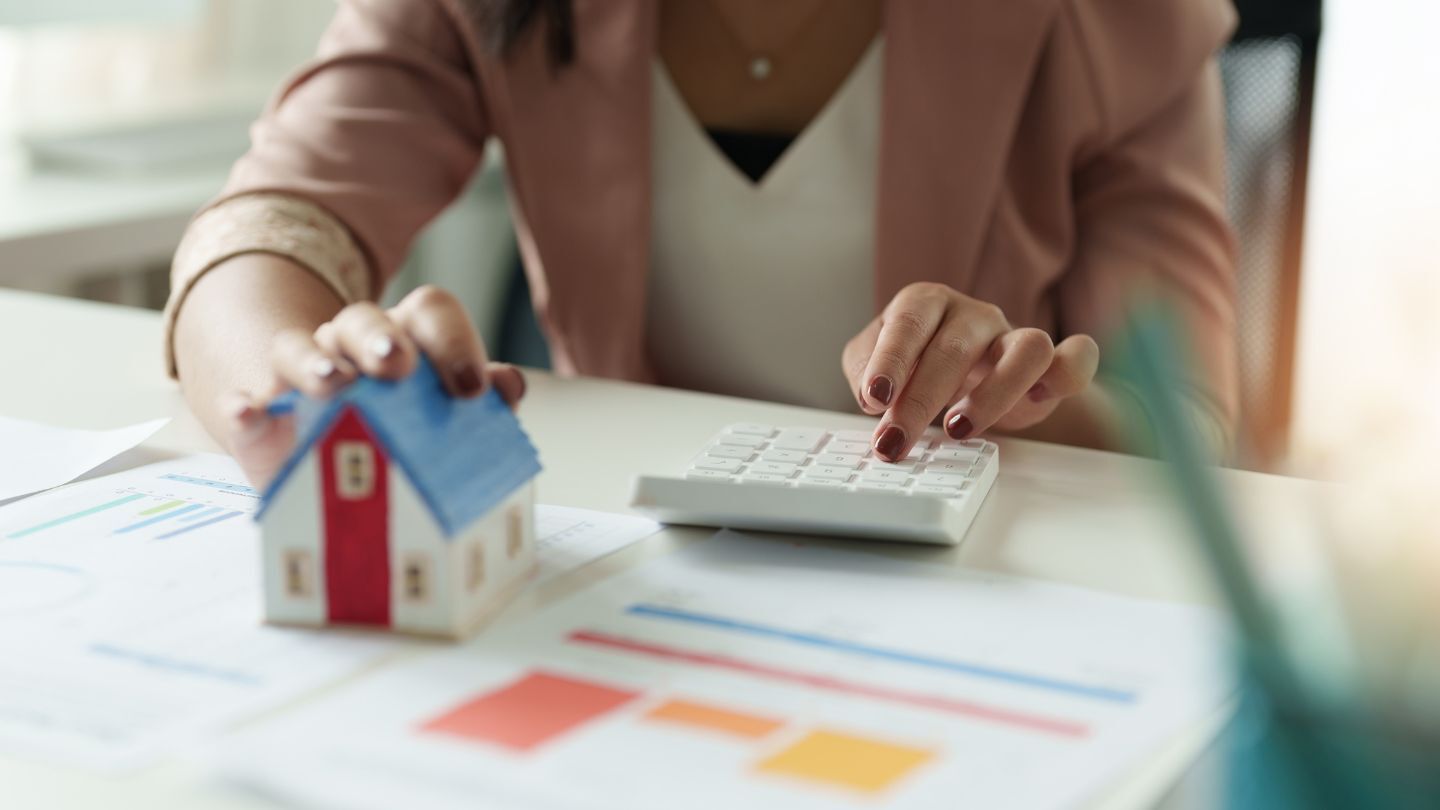 Crédito hipotecario. Mujer usando una calculadora frente a una casa en miniatura